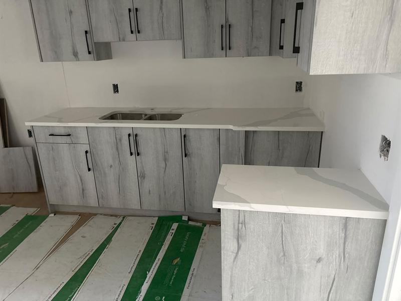 Driftwood grey wood-grain flat-panel cabinets with black handles and white marble-look quartz with a double sink