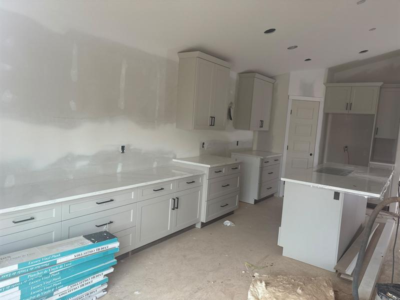 Greige shaker cabinets and drawers with matte black bar pulls and a white quartz counter