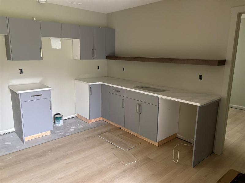 Grey flat-panel kitchenette cabinets with a long walnut floating shelf and white counter
