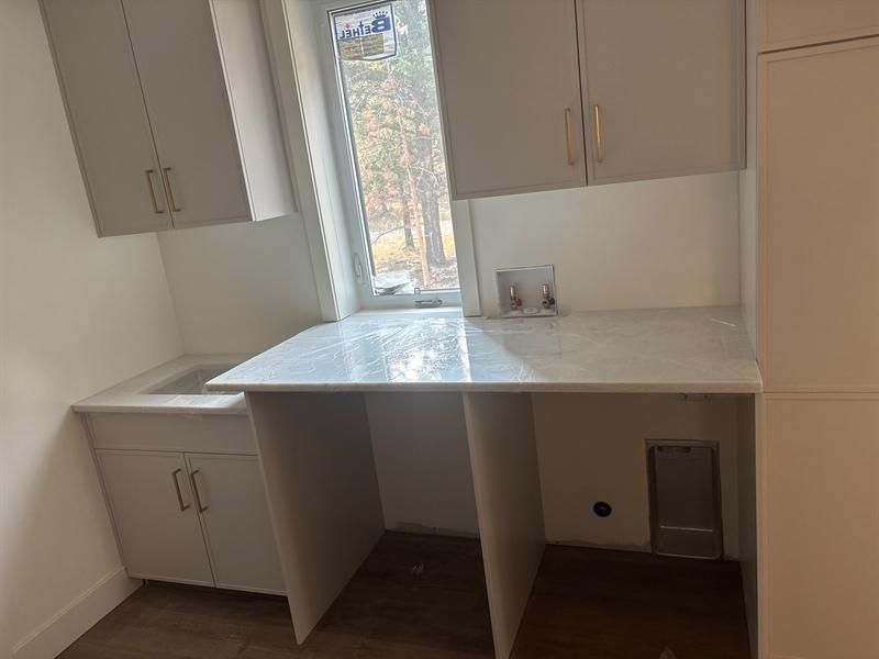 Laundry room with light grey cabinets, brass pulls and a stone folding counter over the washer and dryer space