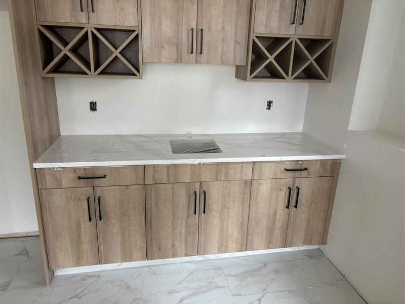 Oak flat-panel bar cabinets with black pulls and X-shaped wine racks above a white counter