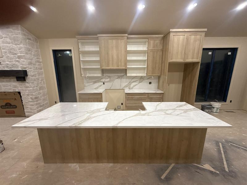 Large oak island topped with white quartz with soft gold veining, oak upper cabinets and full-height quartz backsplash