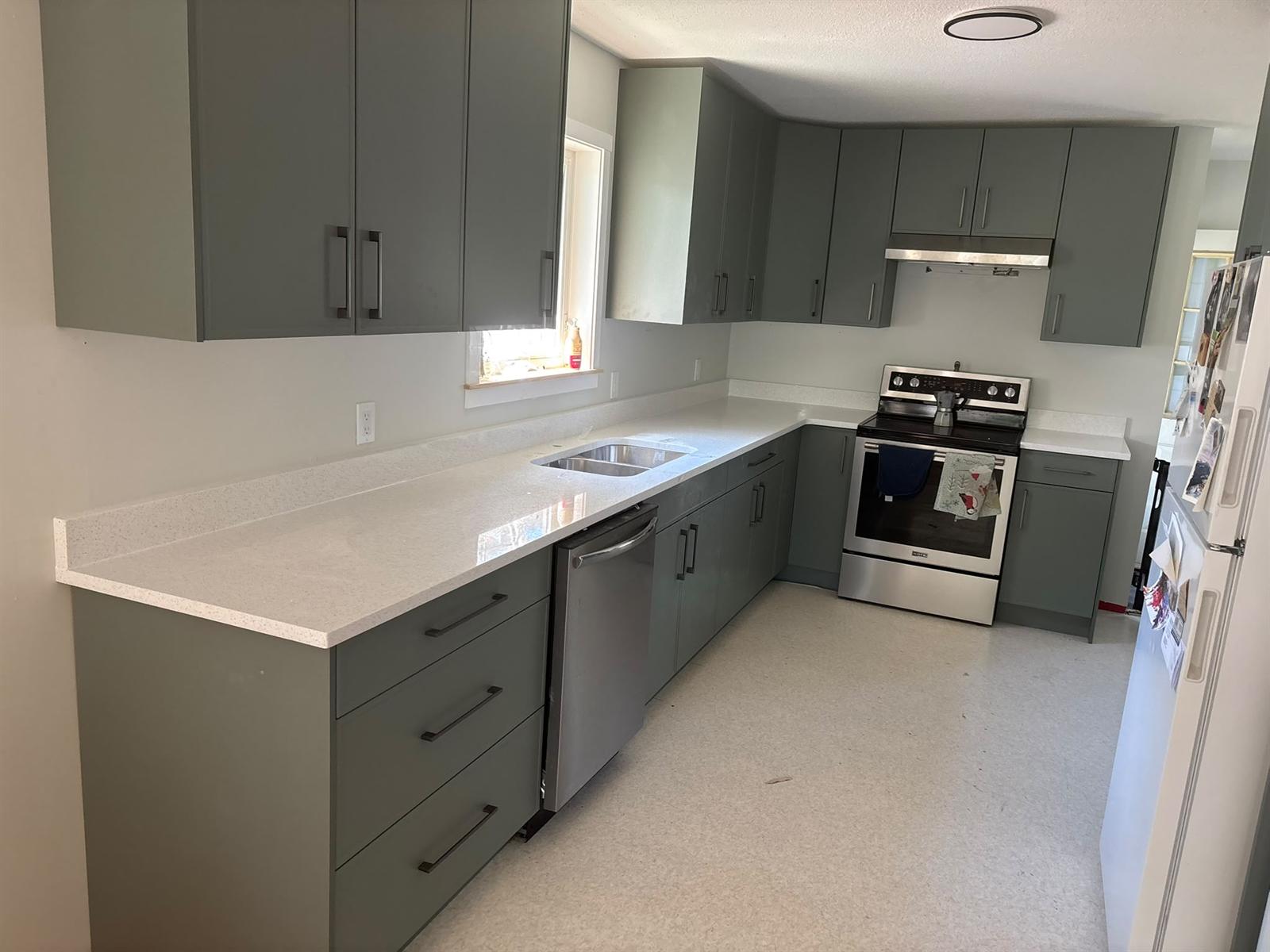 Sage green flat-panel kitchen cabinets with long bar pulls and a sparkling white quartz countertop wrapping an L-shaped layout