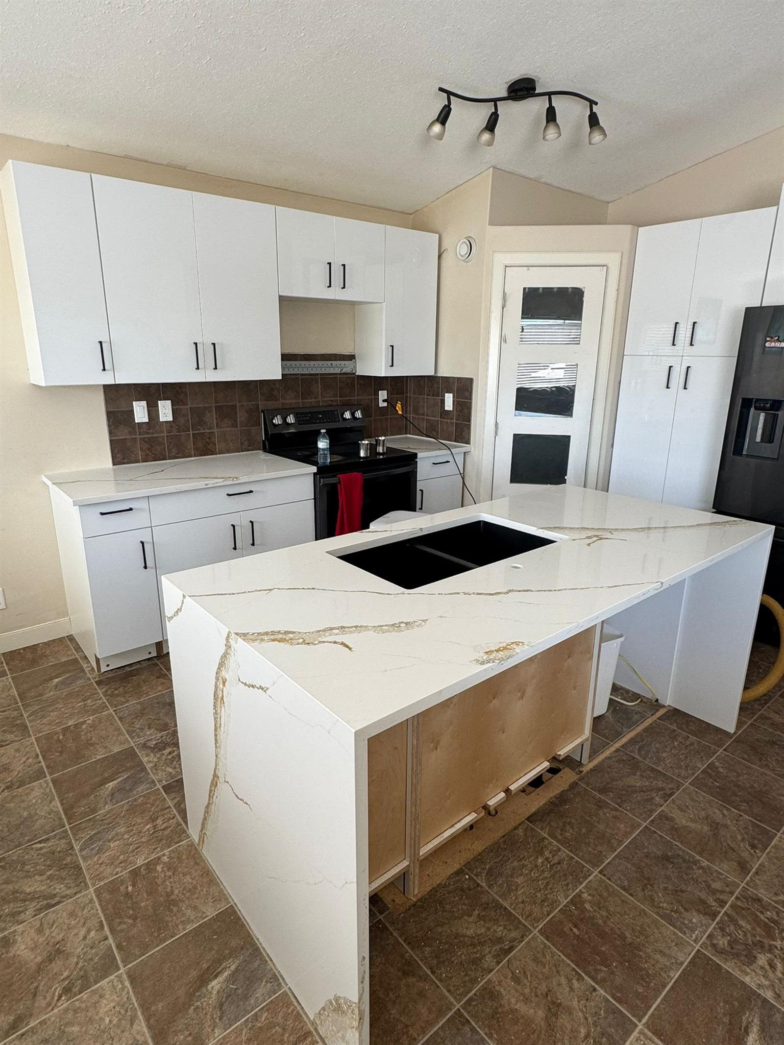 White quartz waterfall island with bold gold and grey veining running down the side, black undermount sink and white cabinets behind