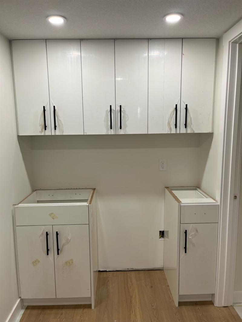 White high-gloss upper and base cabinets with black bar pulls, installed and waiting for countertops