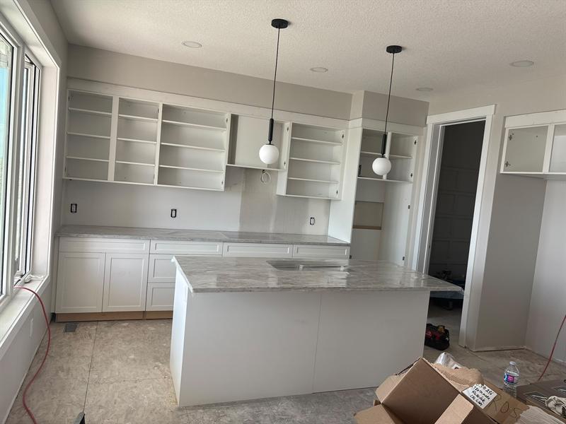 Grey and white veined stone countertops on a white island with sink and white shaker perimeter cabinets