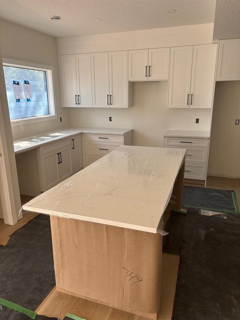 White shaker kitchen with black pulls and a large island topped with white quartz with fine grey veins
