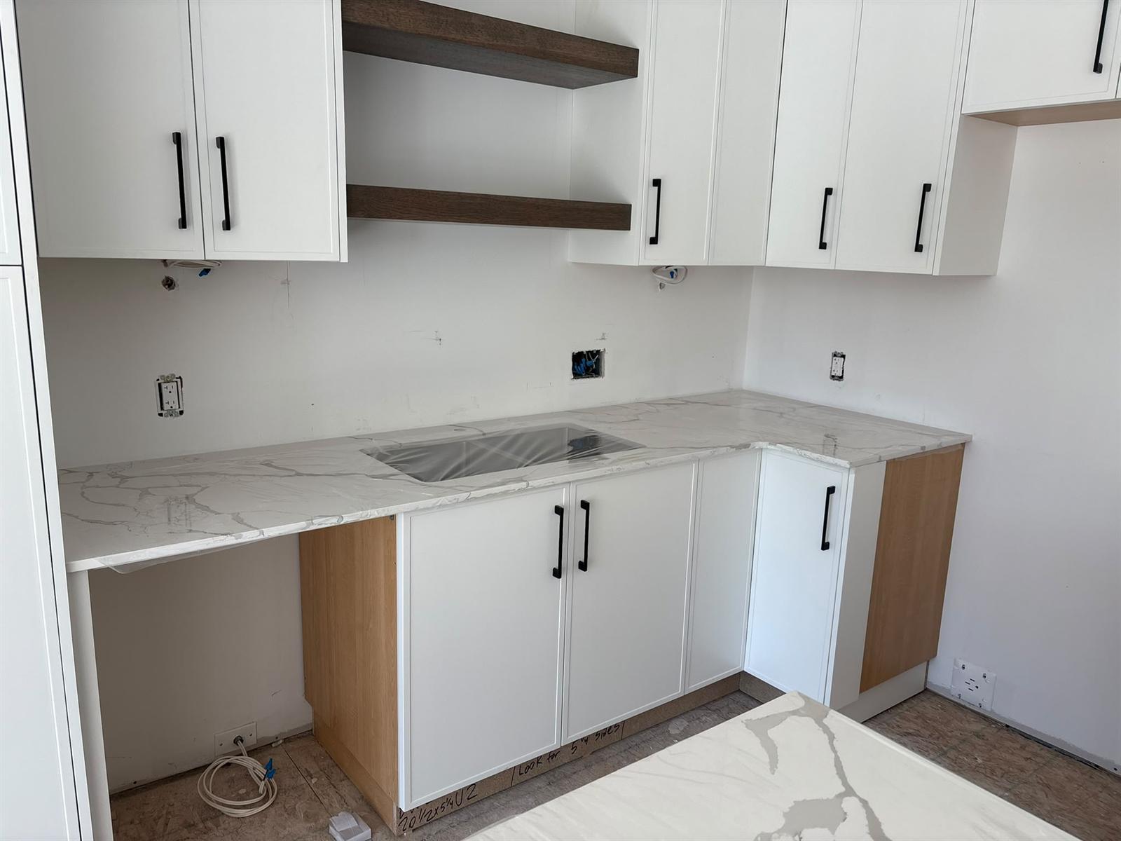 White shaker cabinets beside dark walnut floating shelves above a white marble-look quartz countertop with undermount sink